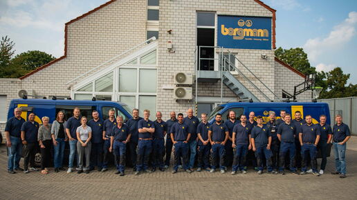 Gruppenfoto des gesamten Borgmann-Teams in Arbeitskleidung vor dem Firmengebäude mit zwei blauen Firmenfahrzeugen